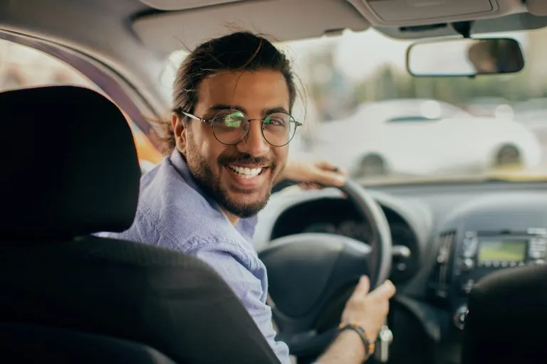 Fröhlicher mittelöstlicher Taxifahrer, der auf den Rücksitz schaut und lächelt